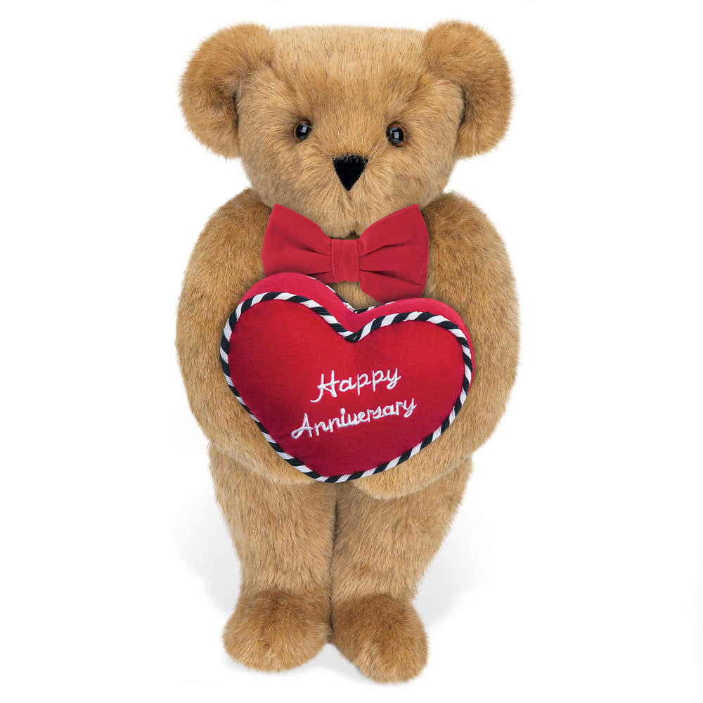 Light brown teddy bear holding red heart pillow with "Happy Anniversary" embroidery and red bow tie.