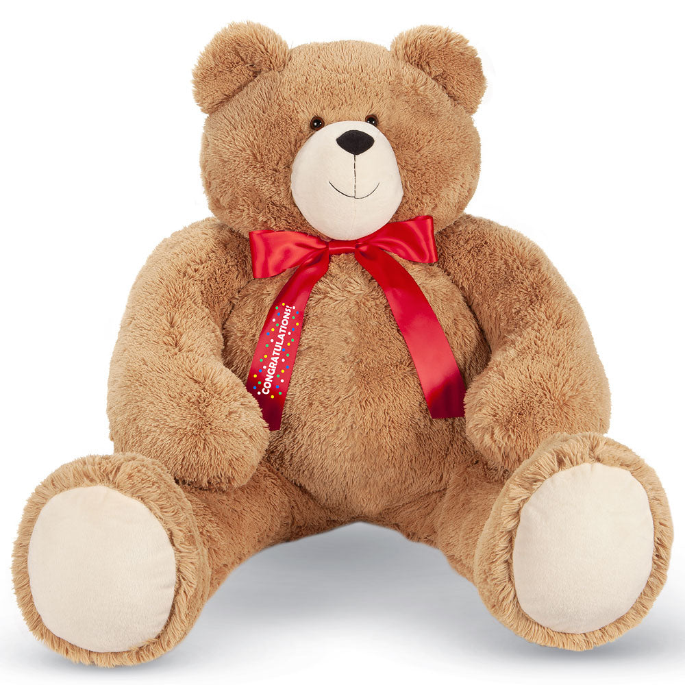 Large plush teddy bear in light brown with a smiling face and a red satin bow with congratulations text.
