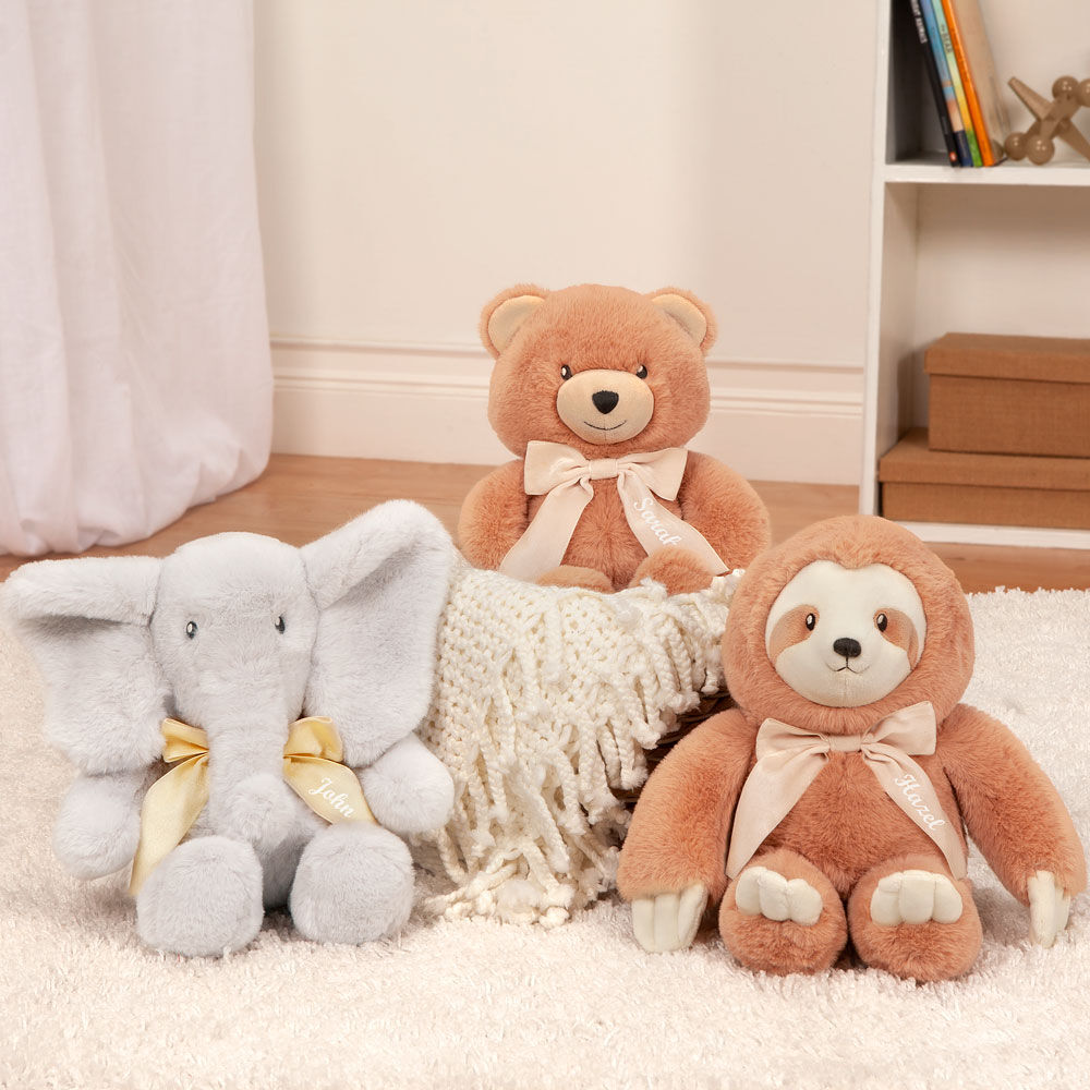 Plush 13-inch sloth with light brown fur and white face sitting on a cream rug next to gray elephant and brown bear stuffed.