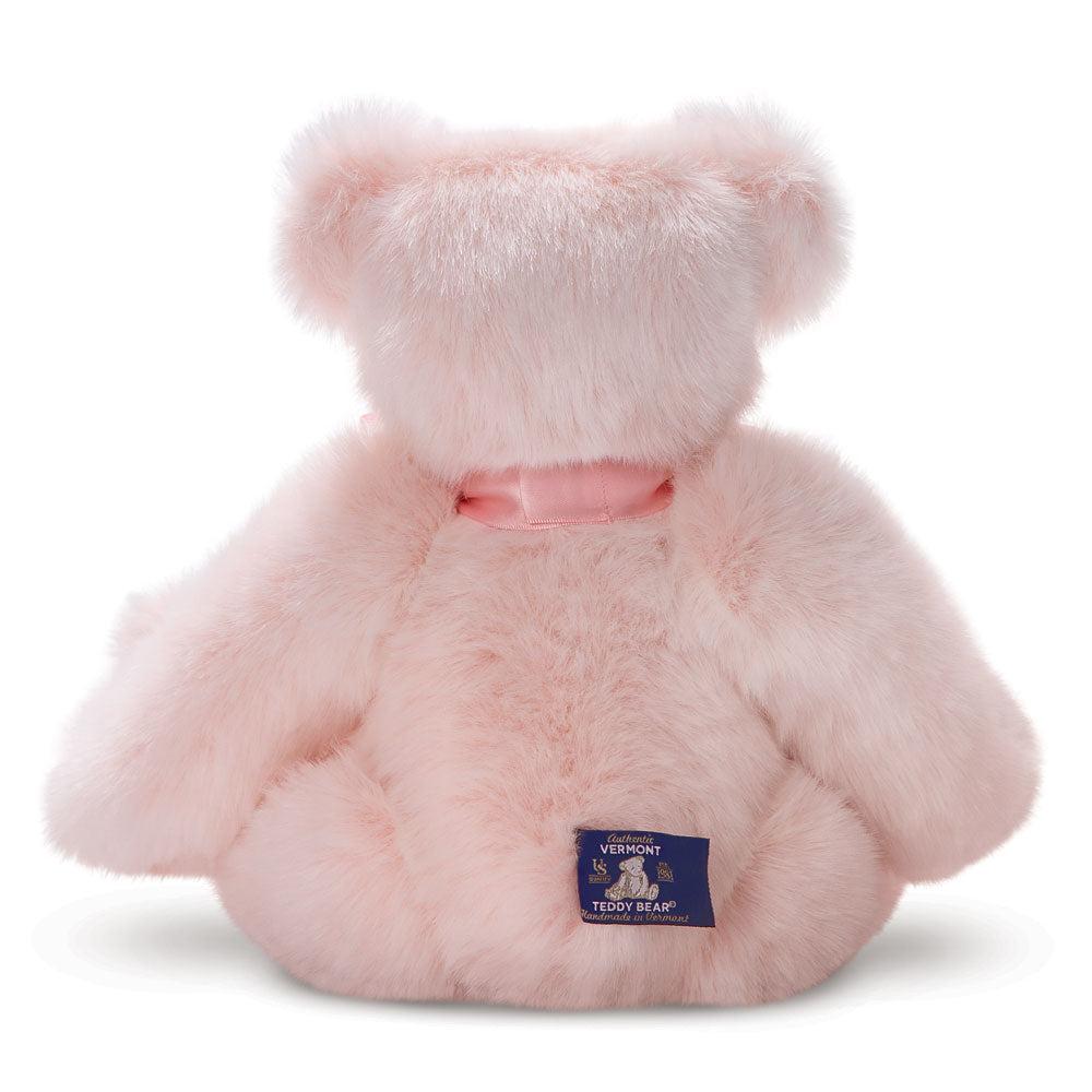 Soft pink premium teddy bear with fluffy fur and a satin ribbon collar, sitting facing backward.