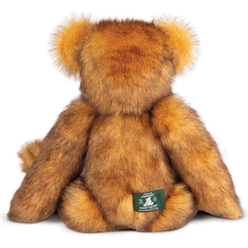Plush brown teddy bear with fluffy ears and a small green tag on its back.