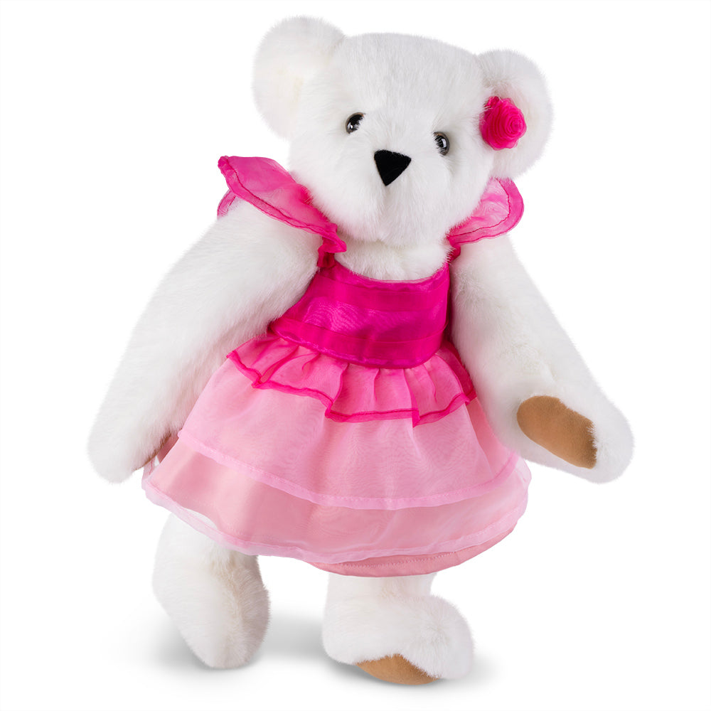 White plush bear with black nose and eyes, wearing layered pink dress and pink flower on ear.