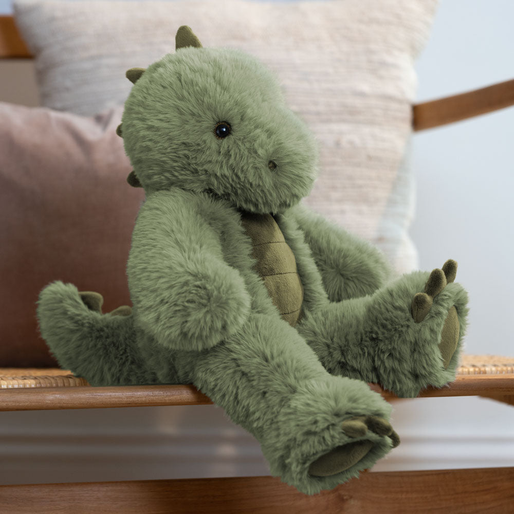 Soft plush green T-Rex dinosaur with stitched details and round black eyes sitting on wooden bench.