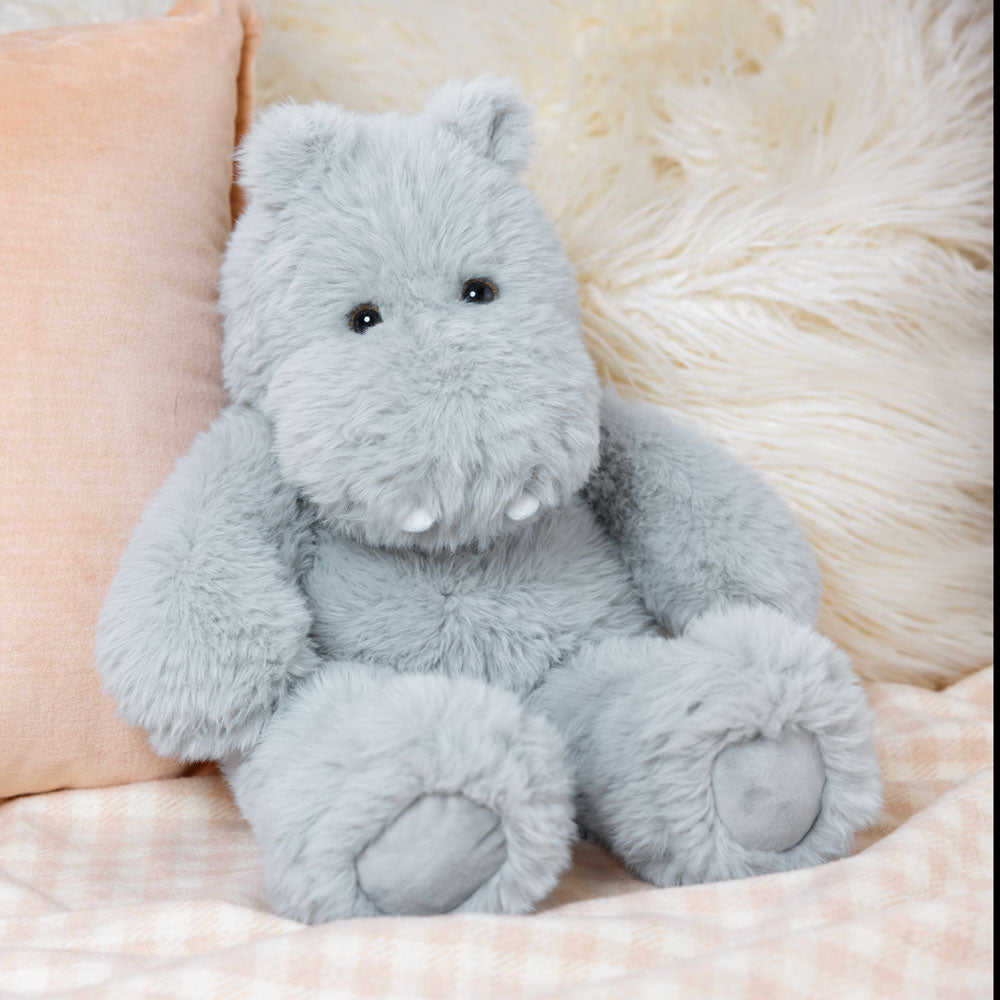 Plush light gray hippo toy with soft fur and stitched details sitting on a beige plaid blanket.
