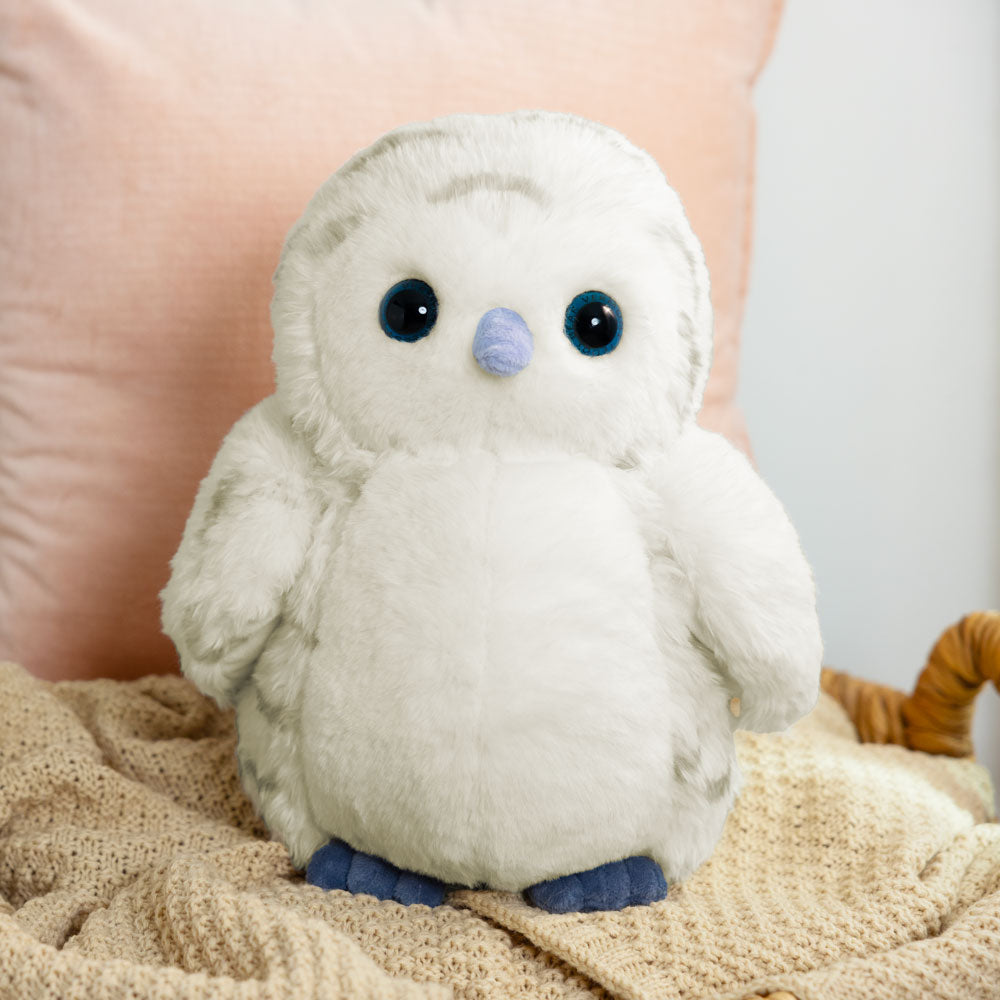 Soft white snowy owl plush with black eyes and blue beak and feet on a knitted blanket.