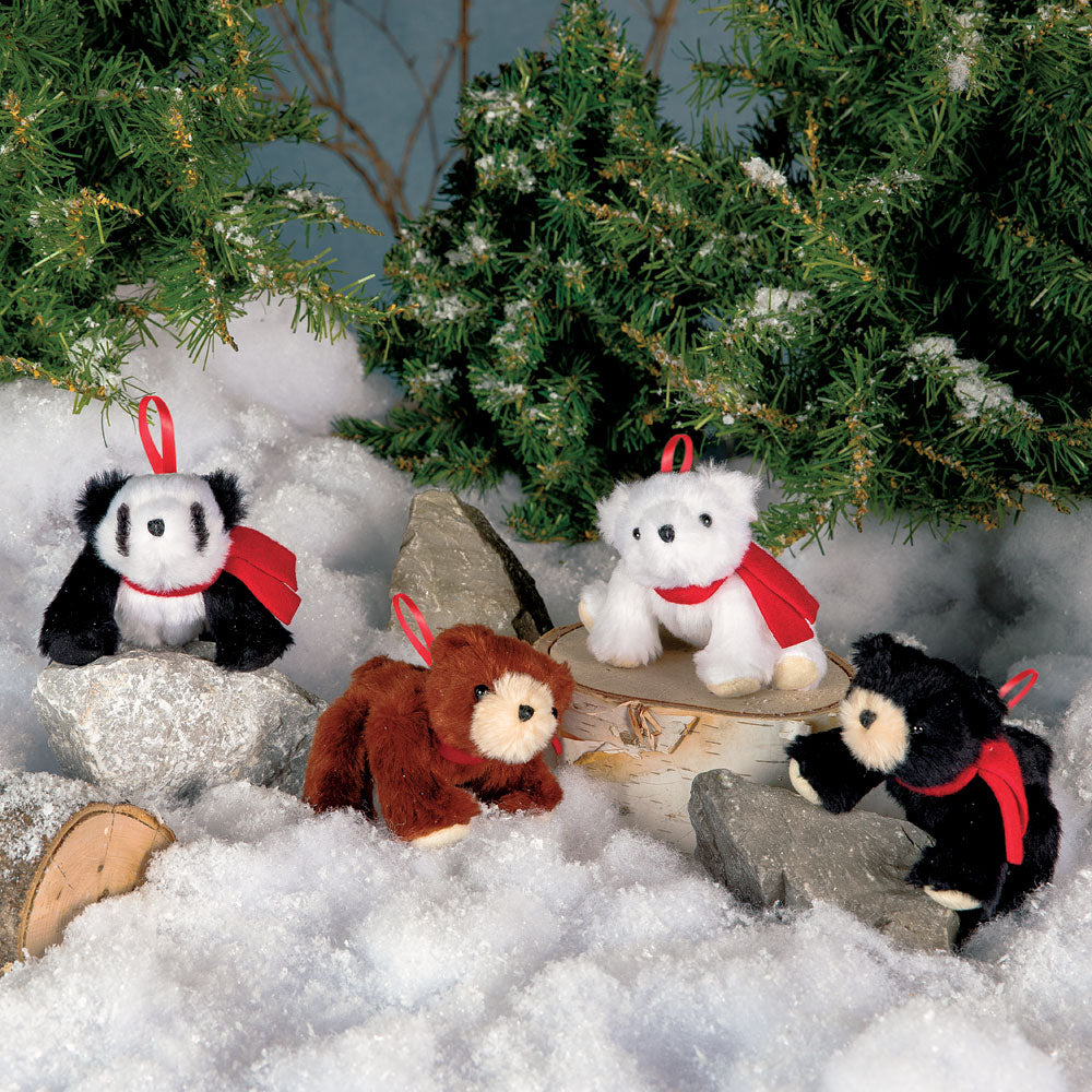 Four plush bear ornaments in black, brown, white, and gray with red scarves on artificial snow under pine trees.