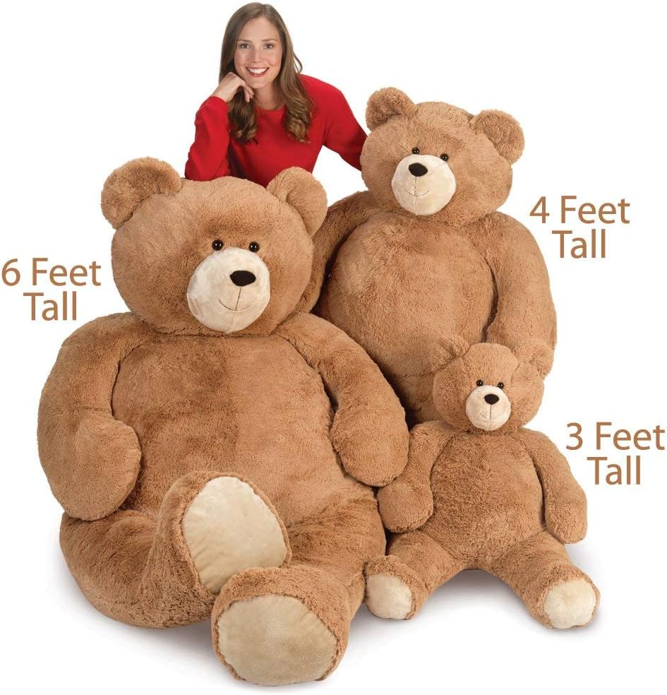 Three brown plush bears in varying sizes, 3, 4, and 6 feet tall, with a woman wearing a red sweater sitting behind the.
