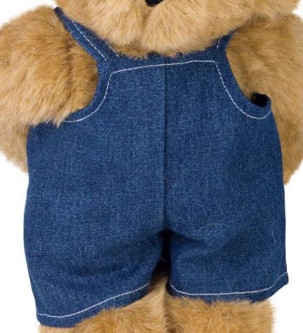 Denim overalls with white stitching on a teddy bear, featuring adjustable shoulder straps and front pocket.