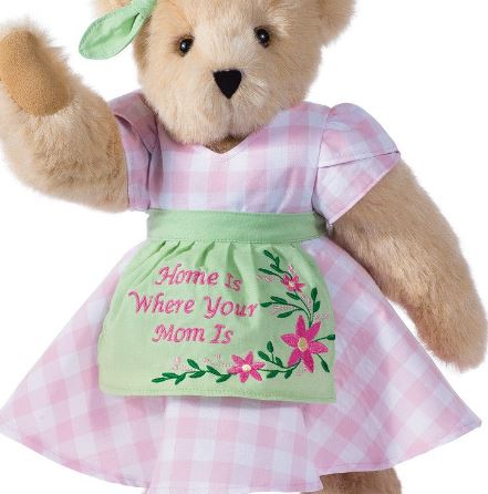 Plush teddy bear wearing pink gingham dress and green apron embroidered with "Home is Where Your Mom Is" and floral design.