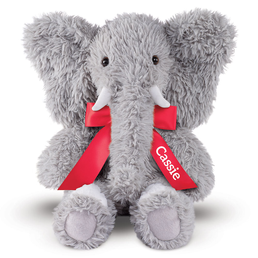Gray plush elephant with large ears, white tusks, and red bow embroidered with "Cassie".