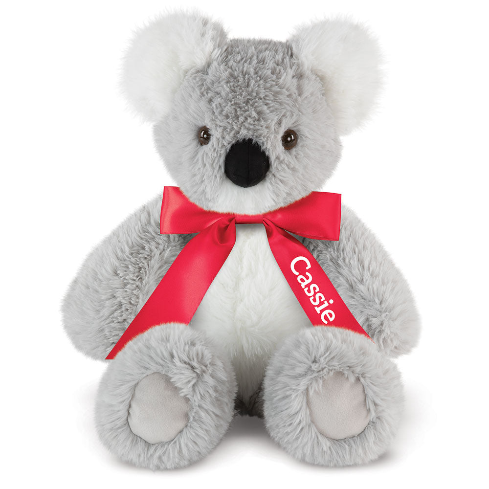 Gray and white plush koala with black nose and eyes, wearing a red bow labeled "Cassie".