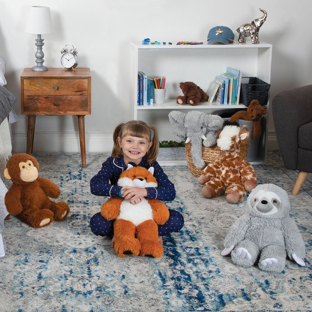 Gray plush sloth toy with smiling face sitting on blue patterned rug next to child and other stuffed animals.
