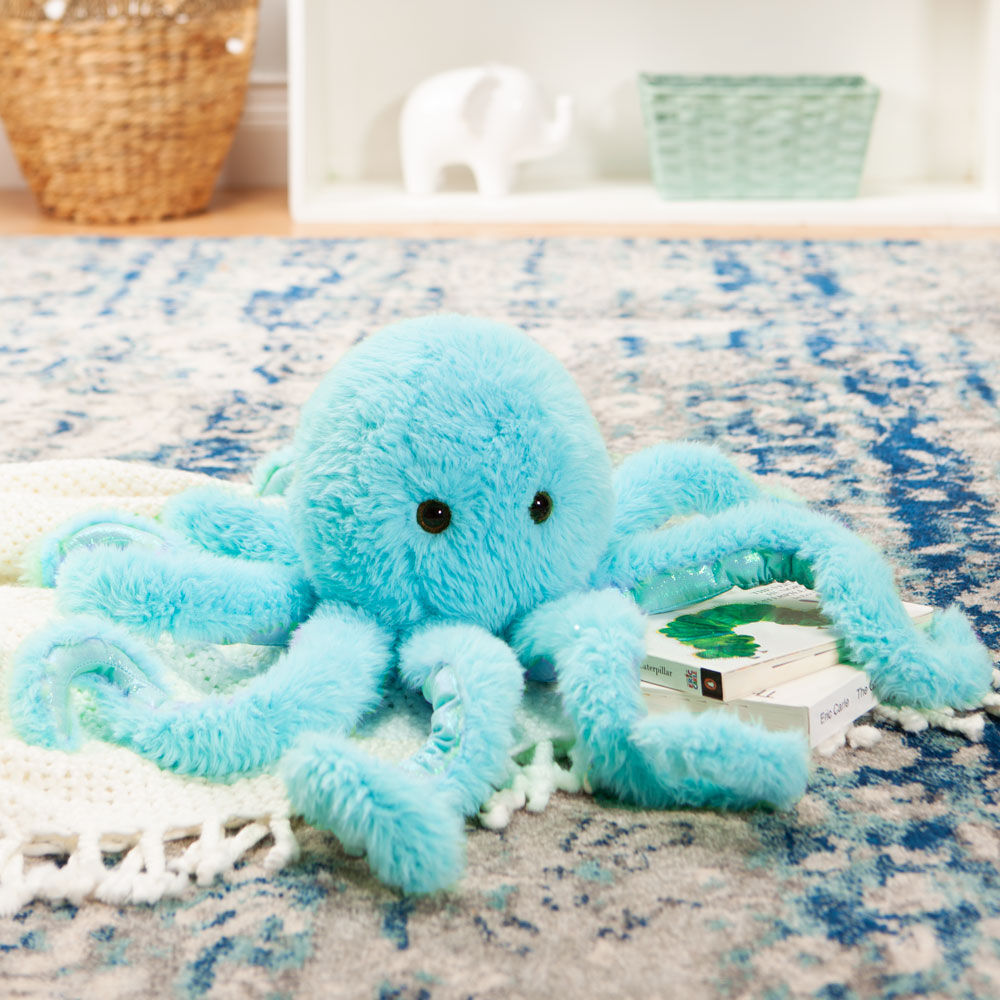 Light blue plush octopus toy with large eyes on a patterned rug next to a small box.