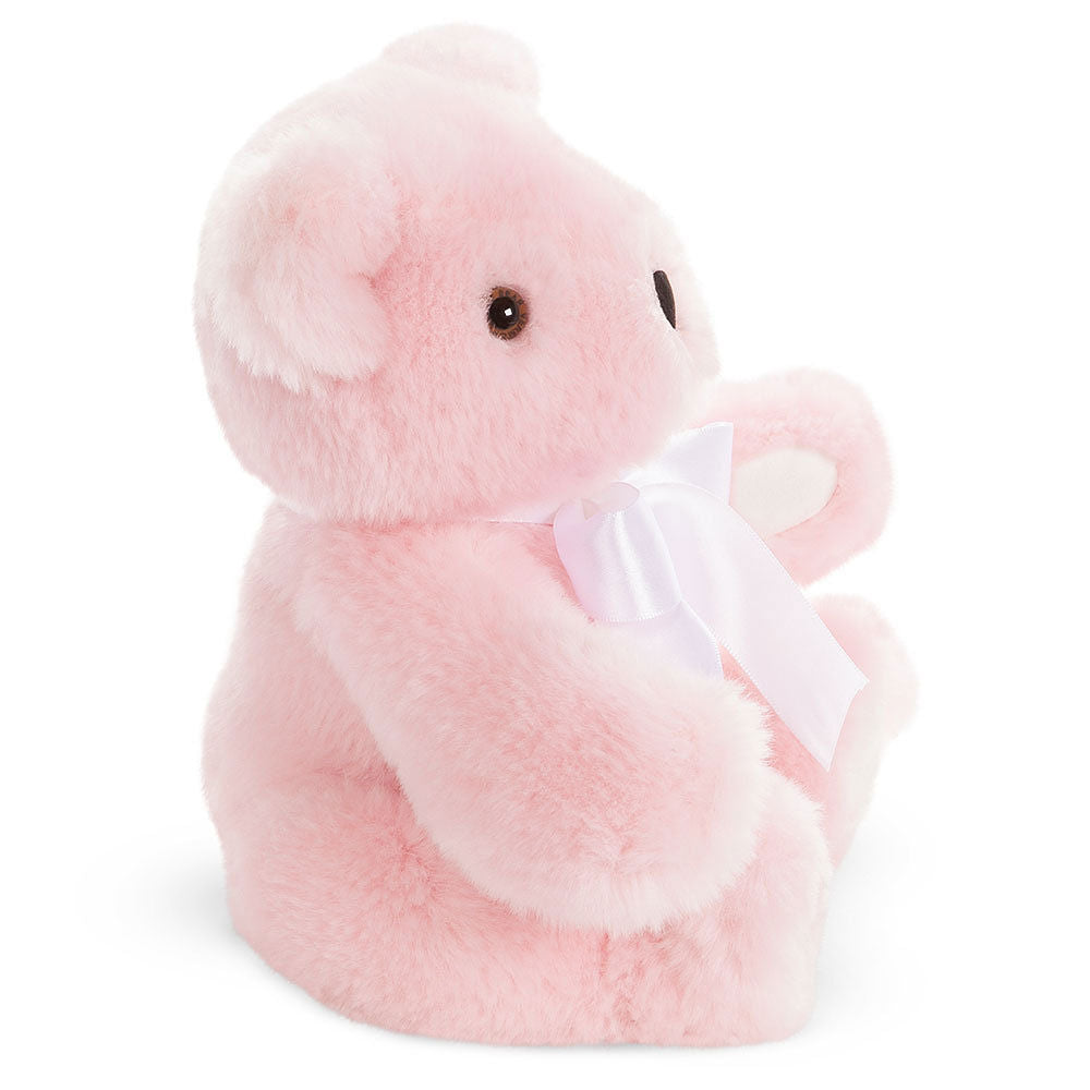 Soft pink plush baby bear with round ears and a white satin bow around its neck, sitting upright.
