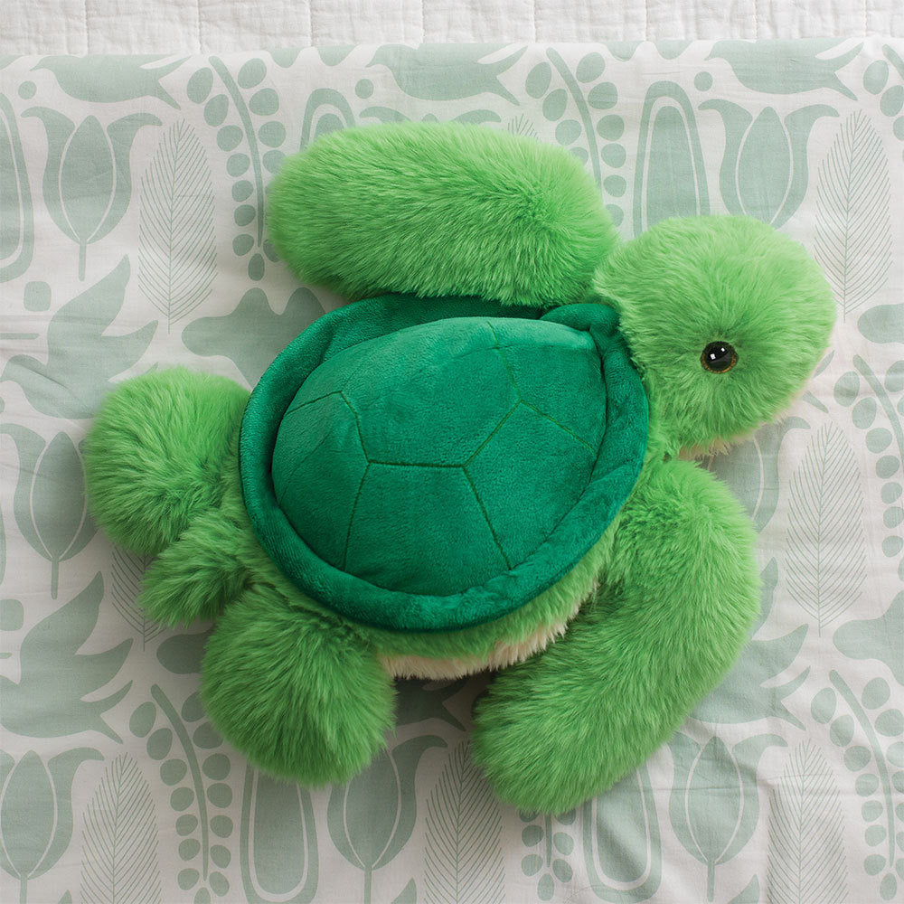Soft plush turtle toy in various shades of green with stitched shell details on a patterned fabric background.