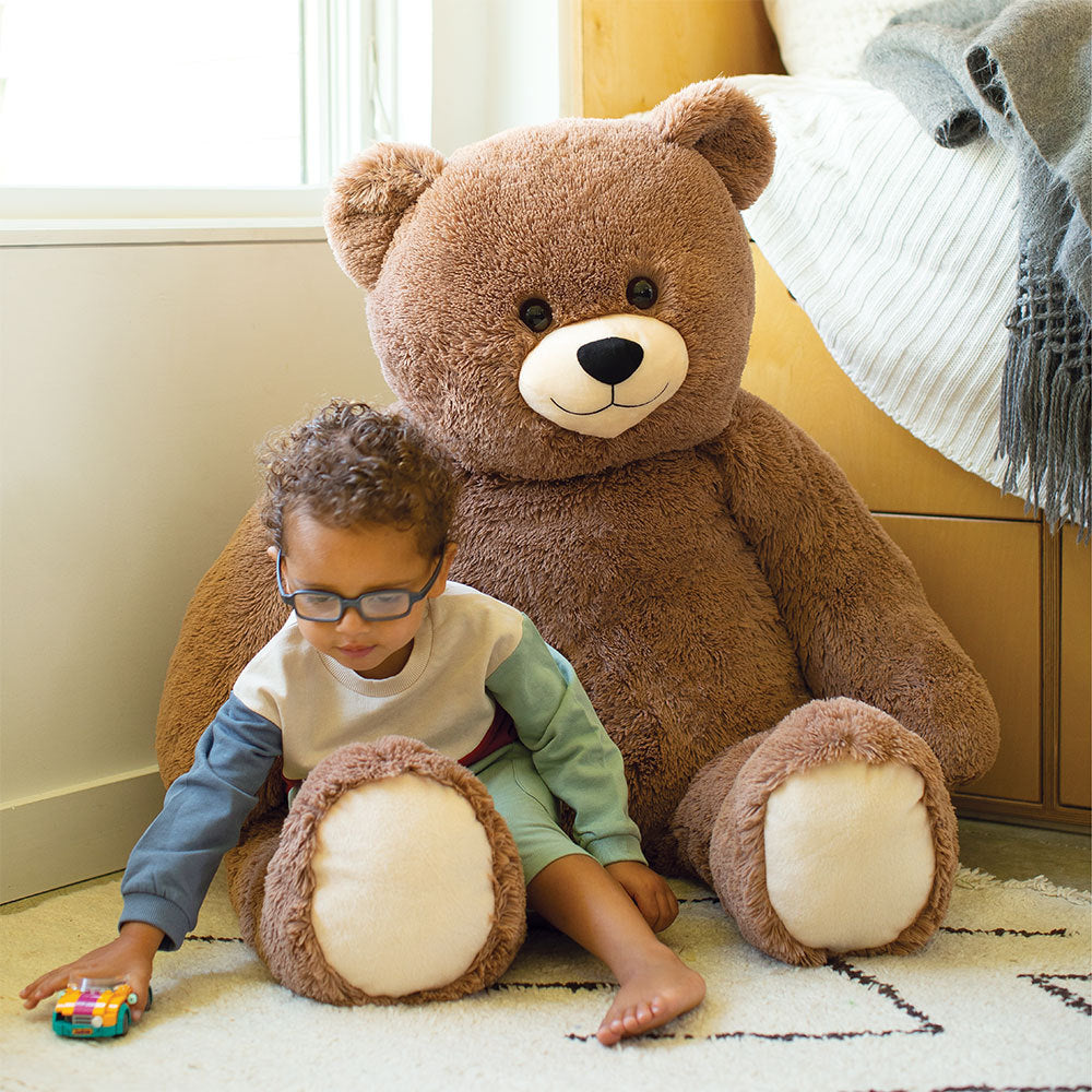 Large 4-foot plush teddy bear in soft brown fur with cream-colored paws and face next to a child playing.