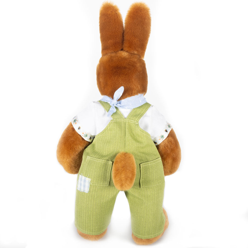 Brown plush bunny wearing white shirt and green overalls with a blue bow on neck, back view.
