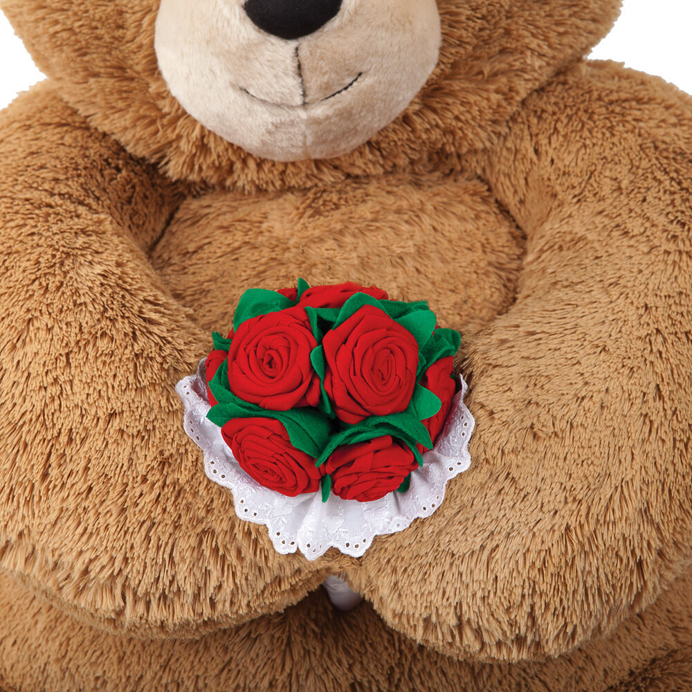 Large plush teddy bear holding a bouquet of red fabric roses with green leaves and white lace trim.