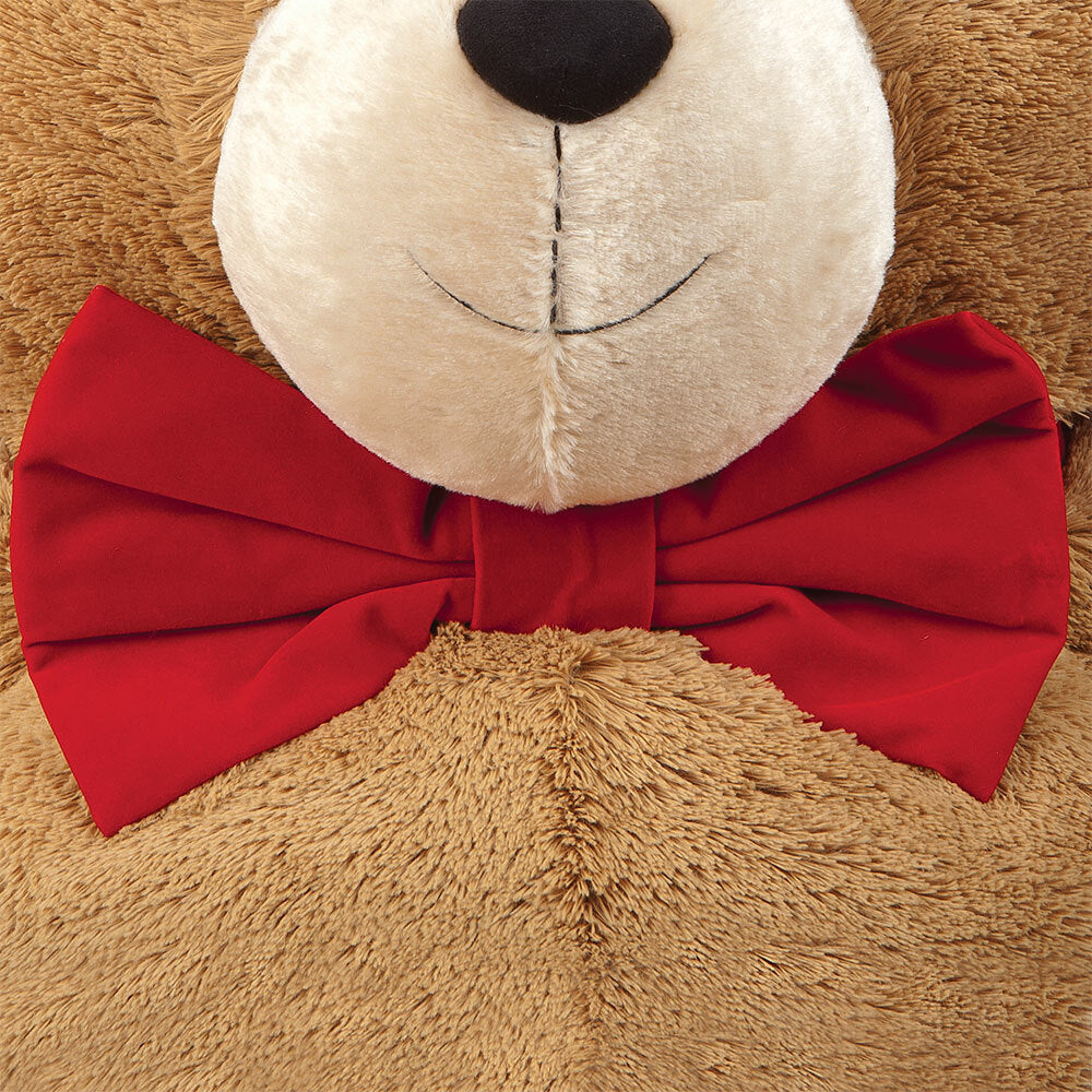Deep red velvet bow tie on light brown plush fabric with a teddy bear face visible above.