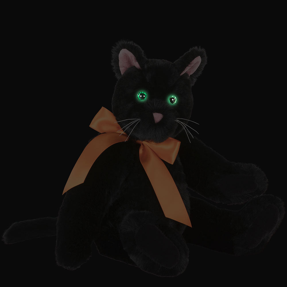 Plush black cat with green eyes and a large orange bow around its neck sitting upright.