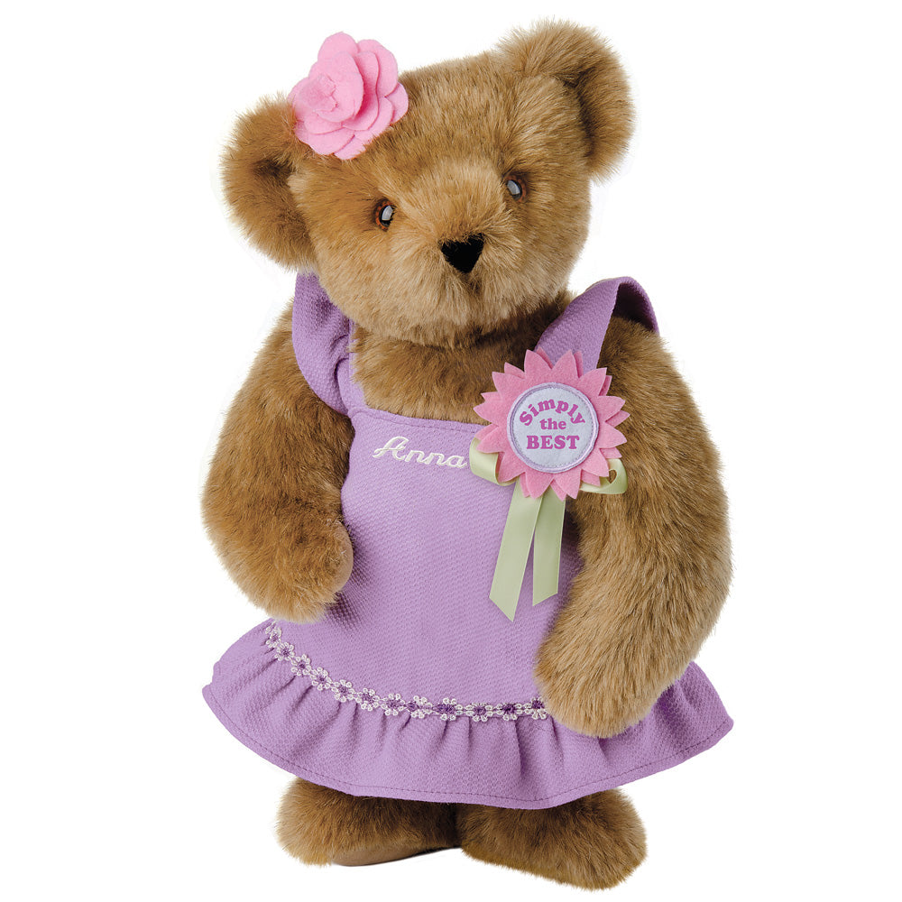 15-inch brown teddy bear wearing a purple dress with a pink flower on its head and a "Simply the Best" badge.