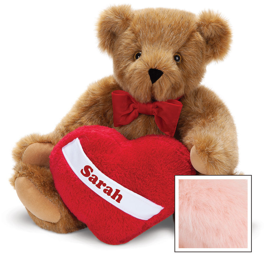 Honey-colored plush teddy bear with brown eyes and red bow tie holding red heart pillow with "Sarah" embroidered.