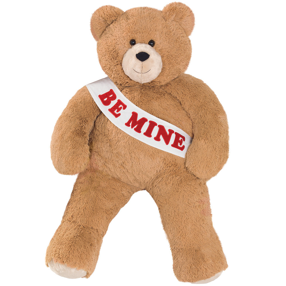 Soft brown plush bear wearing a white sash with "BE MINE" in red letters.