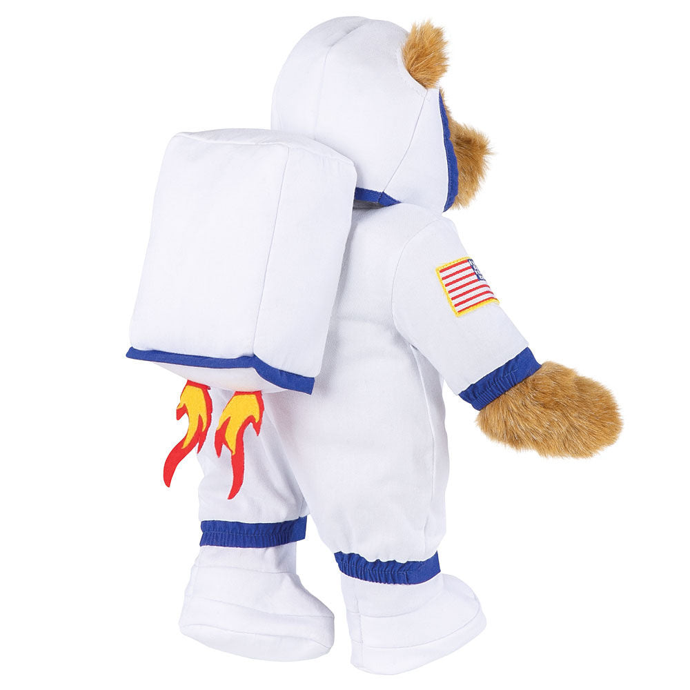 Honey-colored teddy bear in white astronaut suit with American flag patch and rocket flames on backpack.