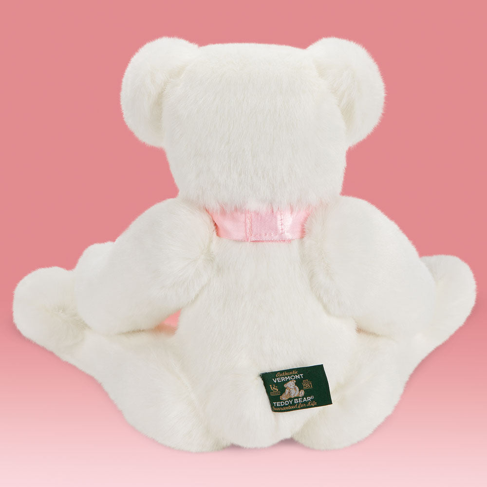 White plush bear with pale pink satin ribbon around neck seated on pink background, green tag on back.