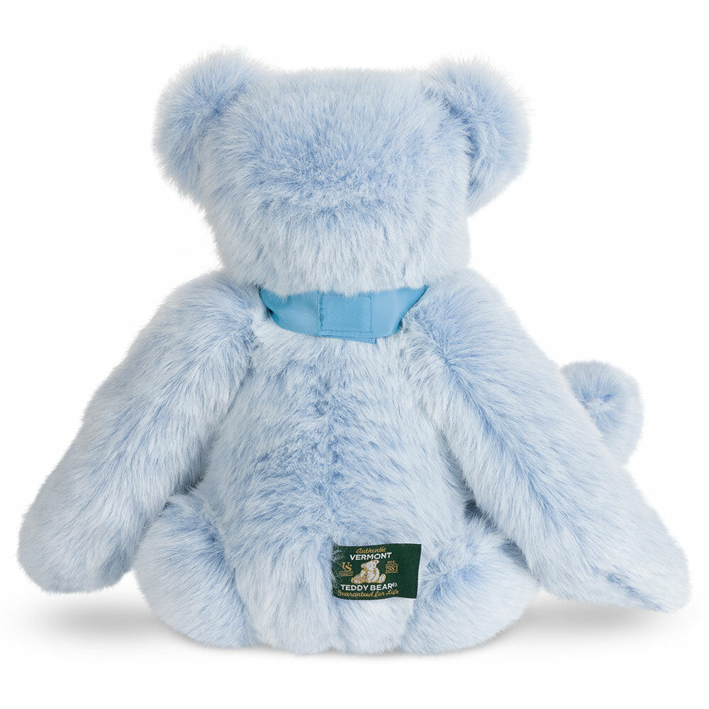 Light blue plush bear with satin blue ribbon bow and sewn green label on back bottom.