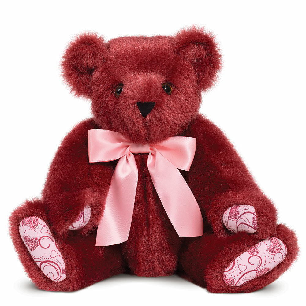 Deep red plush teddy bear with pink heart-patterned paw pads and a pale pink satin bow around its neck.