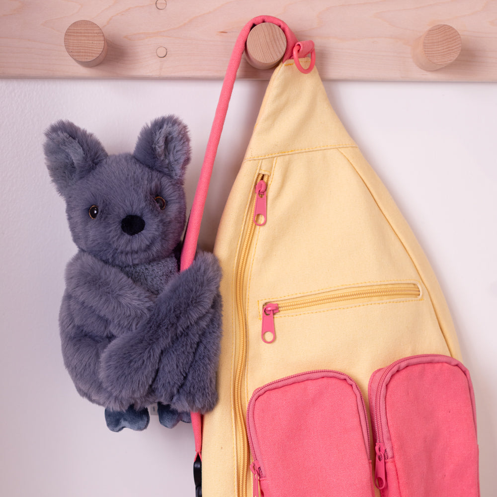 Gray plush bat toy hugging pink and yellow fabric pouch with front pockets and hanging loop.
