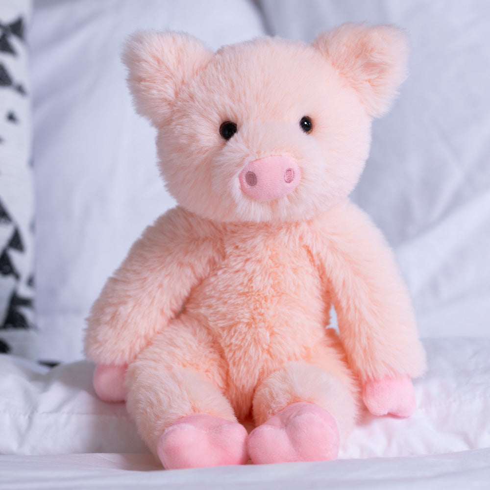 Soft pink plush pig with round black eyes and a stitched snout, sitting upright on a white quilted background.