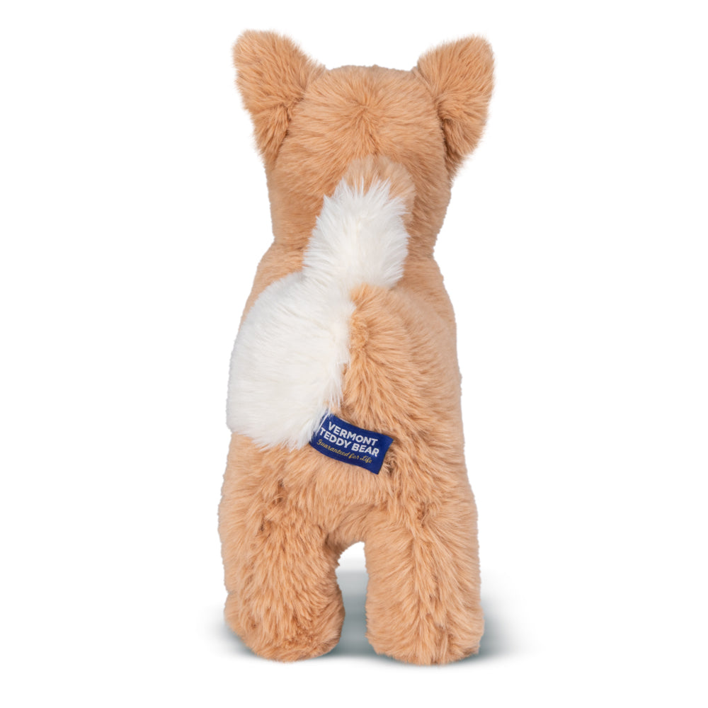 A plush dog toy photographed from the back. The toy is tan/light brown with a white tail, and a blue fabric brand tag near the base of the tail reads VERMONT TEDDY BEAR and Guaranteed for Life.