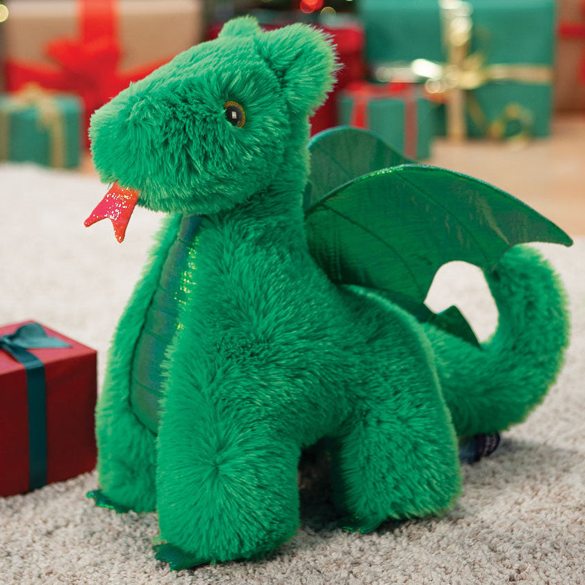 Green plush dragon toy in front of a Christmas tree and presents
