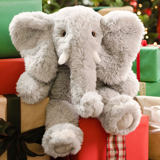 Two plush elephant toys on a stack of Christmas presents with a decorated tree in the background.