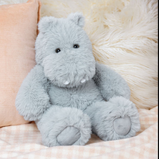 Plush light gray hippo toy with soft fur and stitched details sitting on a beige plaid blanket.