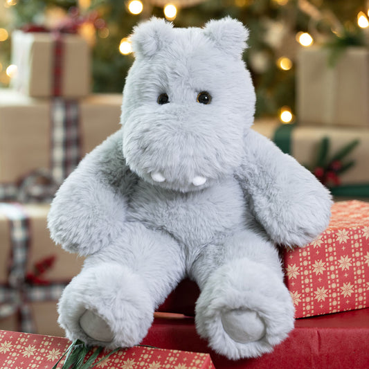 Plush hippo toy on a red surface with Christmas decorations in the background