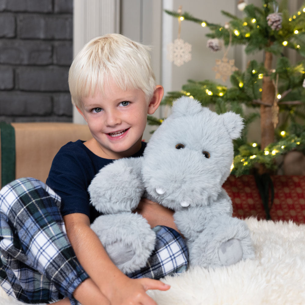 Child holding a plush hippo toy in front of a decorated Christmas tree.