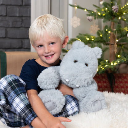 Child holding a plush hippo toy in front of a decorated Christmas tree.