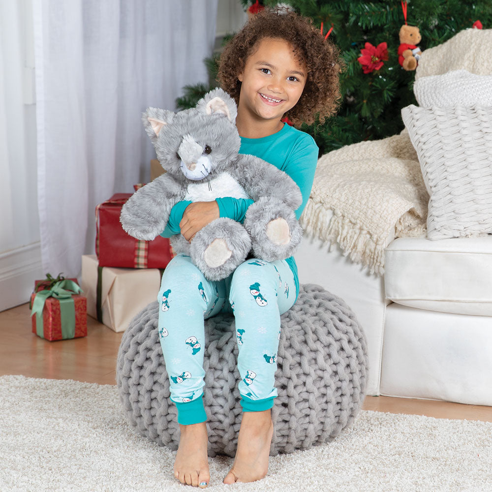 Child holding a plush toy in front of a Christmas tree with presents.