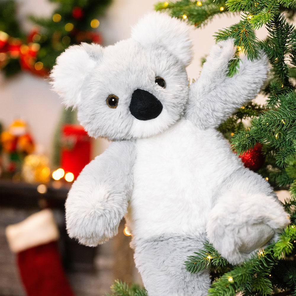 White koala plush toy in front of a decorated Christmas tree with lights and ornaments.