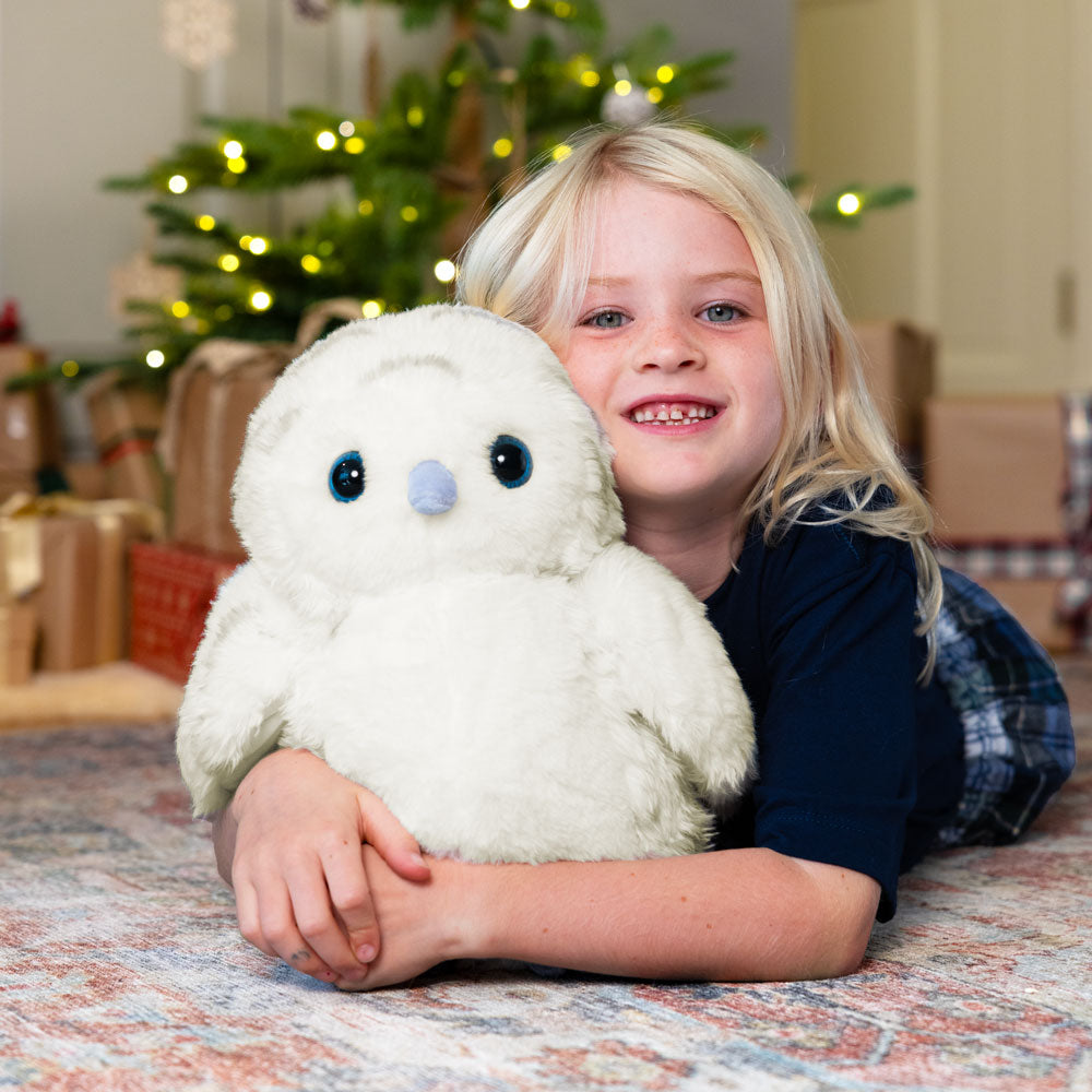 Child holding a white snowy owl stuffed animal in front of a decorated Christmas tree.