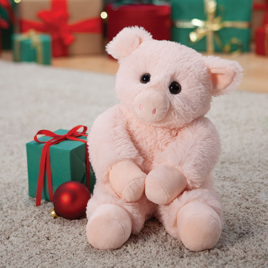 Pink teddy bear sitting on a carpet with Christmas presents and decorations in the background