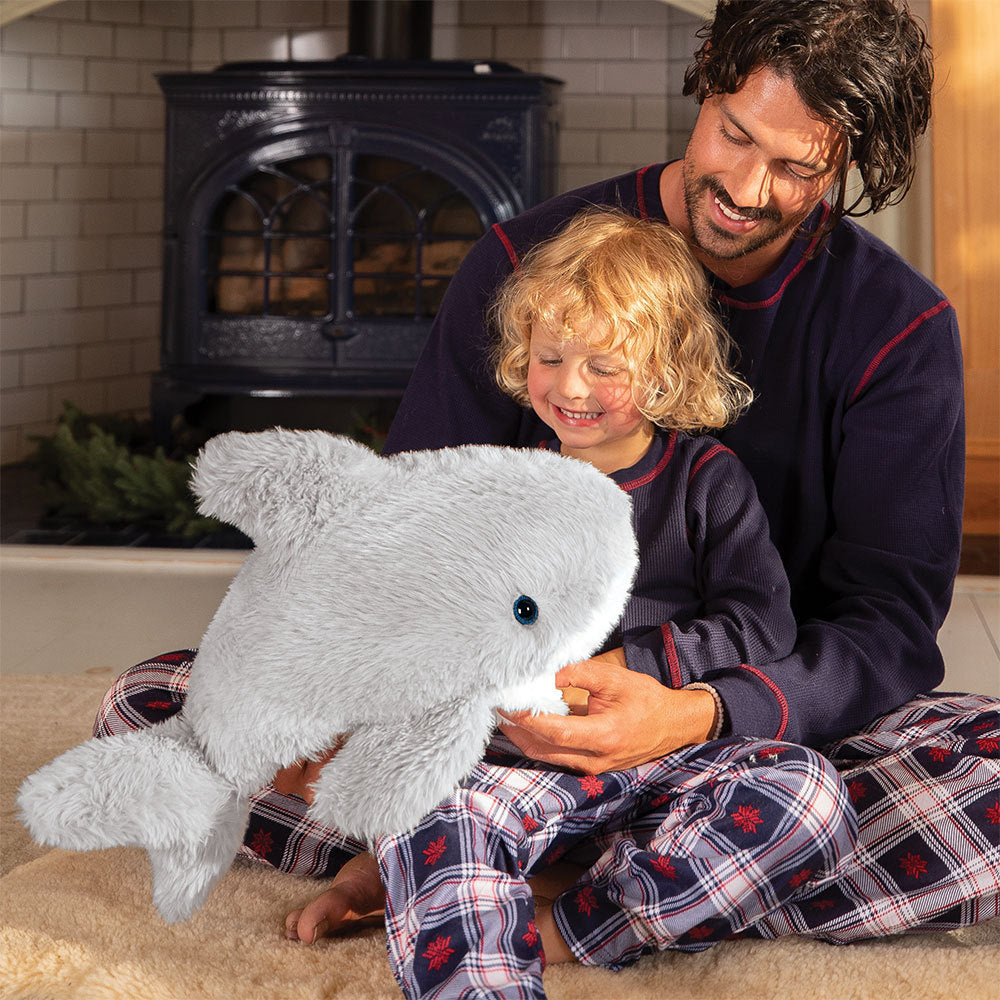 Man and child sitting on the floor with a plush shark toy in front of a fireplace.