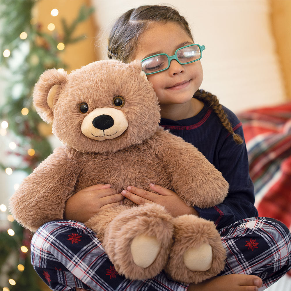 Child holding a stuffed teddy bear toy with a Christmas tree in the background