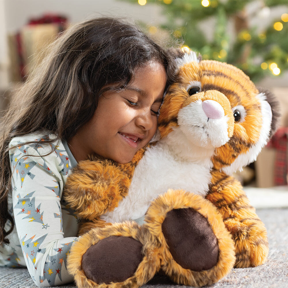 Child holding a plush tiger toy with Christmas gifts in the background