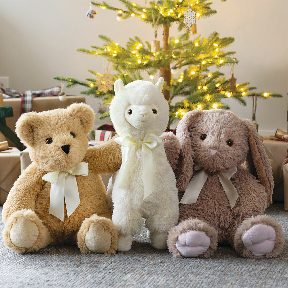 Three plush toys (bear, llama, and rabbit) with ribbons in front of a decorated Christmas tree.