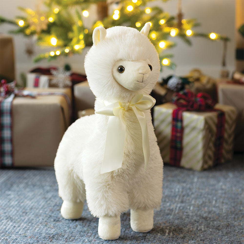 Plush toy llama with a bow in a festive setting with Christmas decorations and presents.