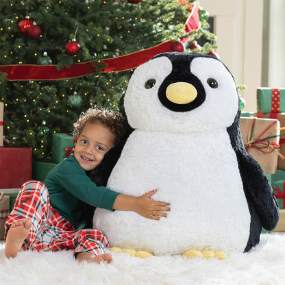 Child hugging a large plush penguin in front of a decorated Christmas tree.